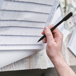 A close-up of a person holding a pen reviewing a financial document with cash visible, ideal for business themes.