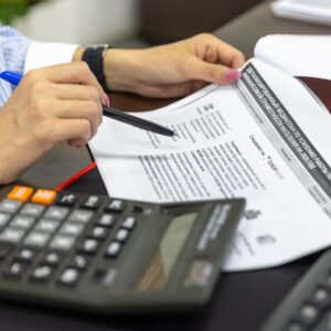 Close-up of a person analyzing financial documents using a calculator and pen.