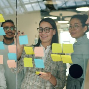 Diverse colleagues collaborating in an office using sticky notes on glass wall.