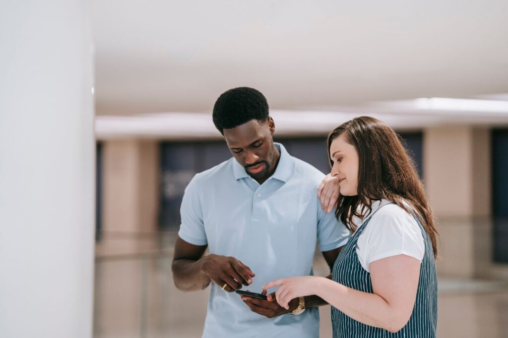 A couple indoors discussing something on a smartphone with focused expressions.