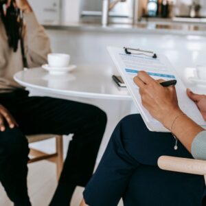 Crop unrecognizable female psychotherapist or interviewer asking questions and taking notes in clipboard during interview with black male