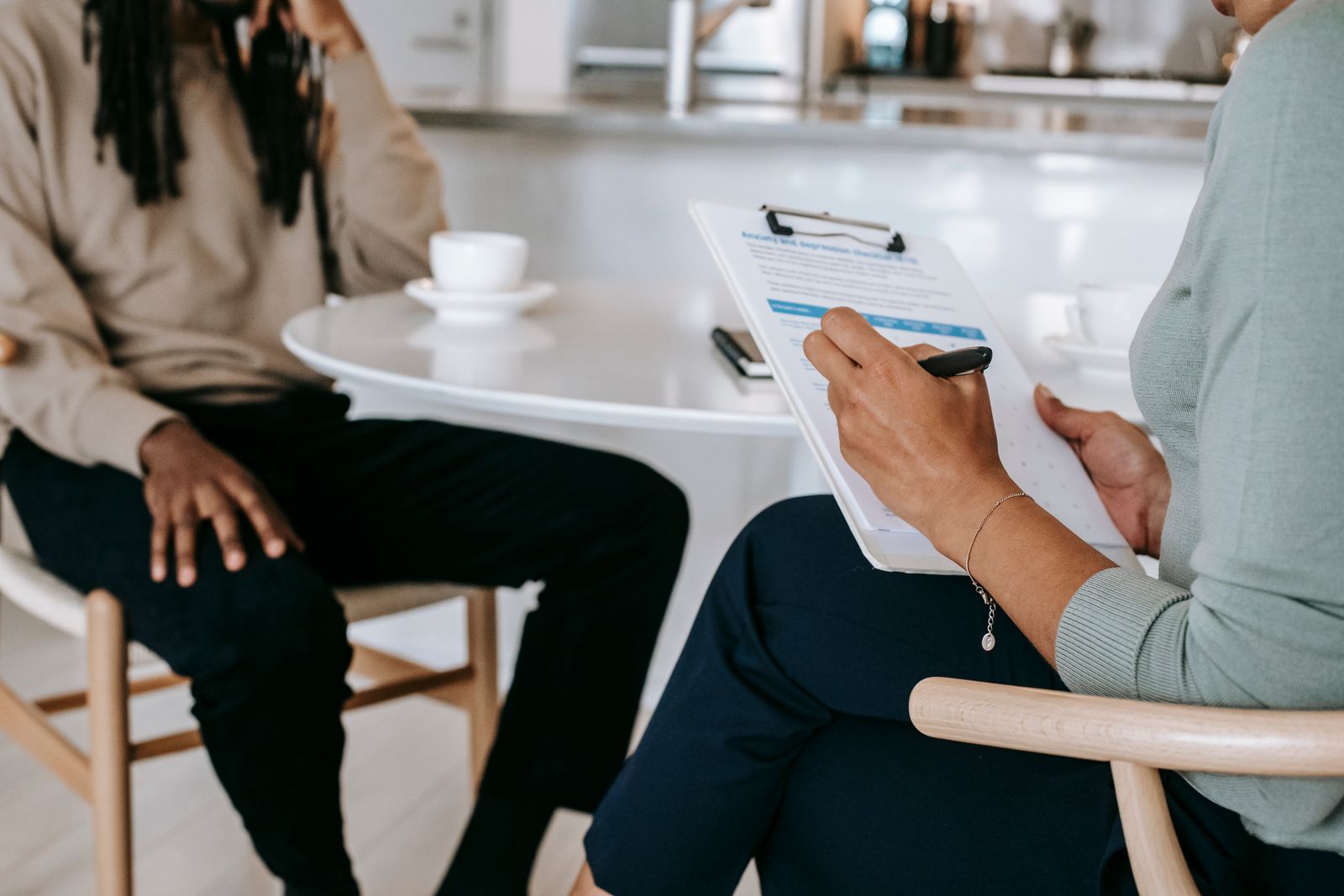 Crop unrecognizable female psychotherapist or interviewer asking questions and taking notes in clipboard during interview with black male
