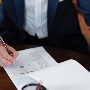 A professional individual signs legal documents at a desk in an office setting.