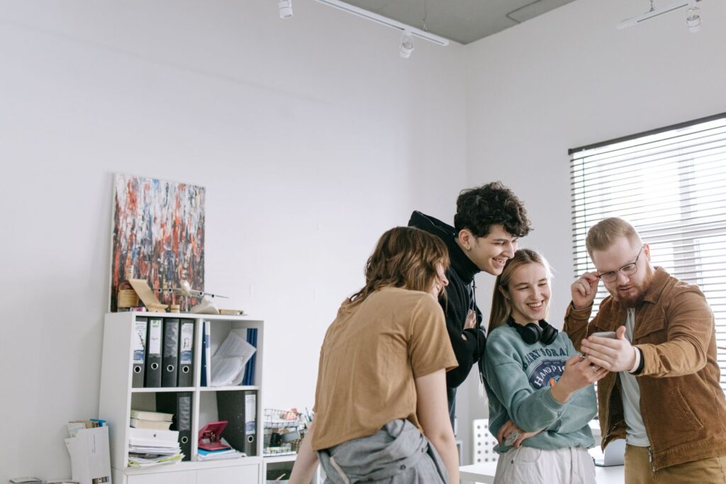 A group of young adults smiling and enjoying a moment together in a bright, modern office environment.