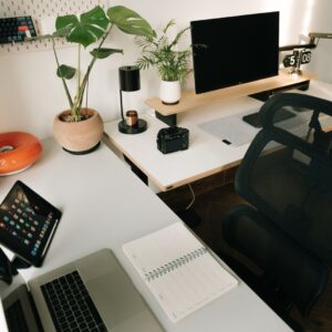 A stylish home office setup featuring tech gadgets, a monitor, a tablet, and decorative plants in a minimalist design.