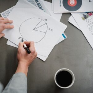 Man drawing a pie chart on paper with coffee, representing business planning and analysis.